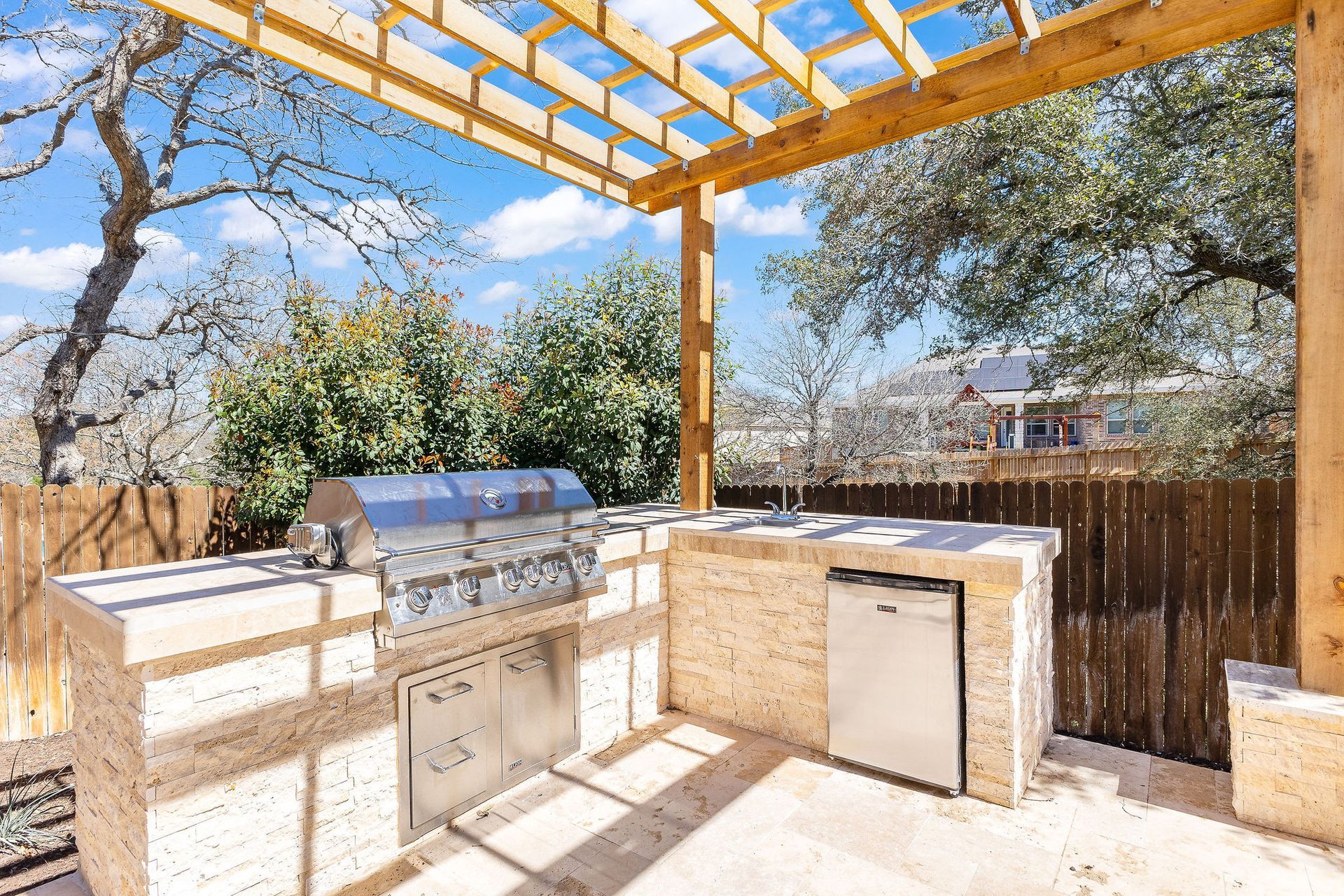 Outdoor patio with built-in grill and counter under a wooden pergola in a sunny backyard