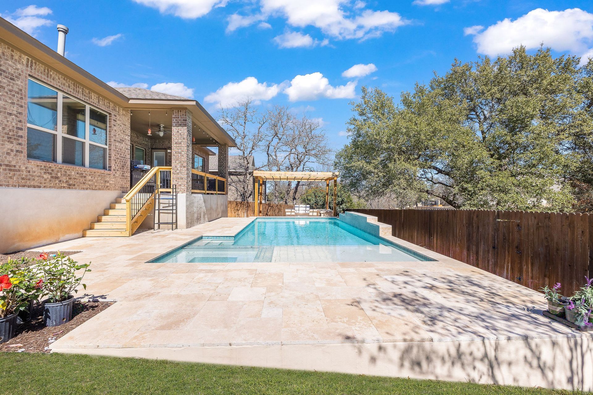 Backyard patio with a rectangular swimming pool beside a two-story house and trees