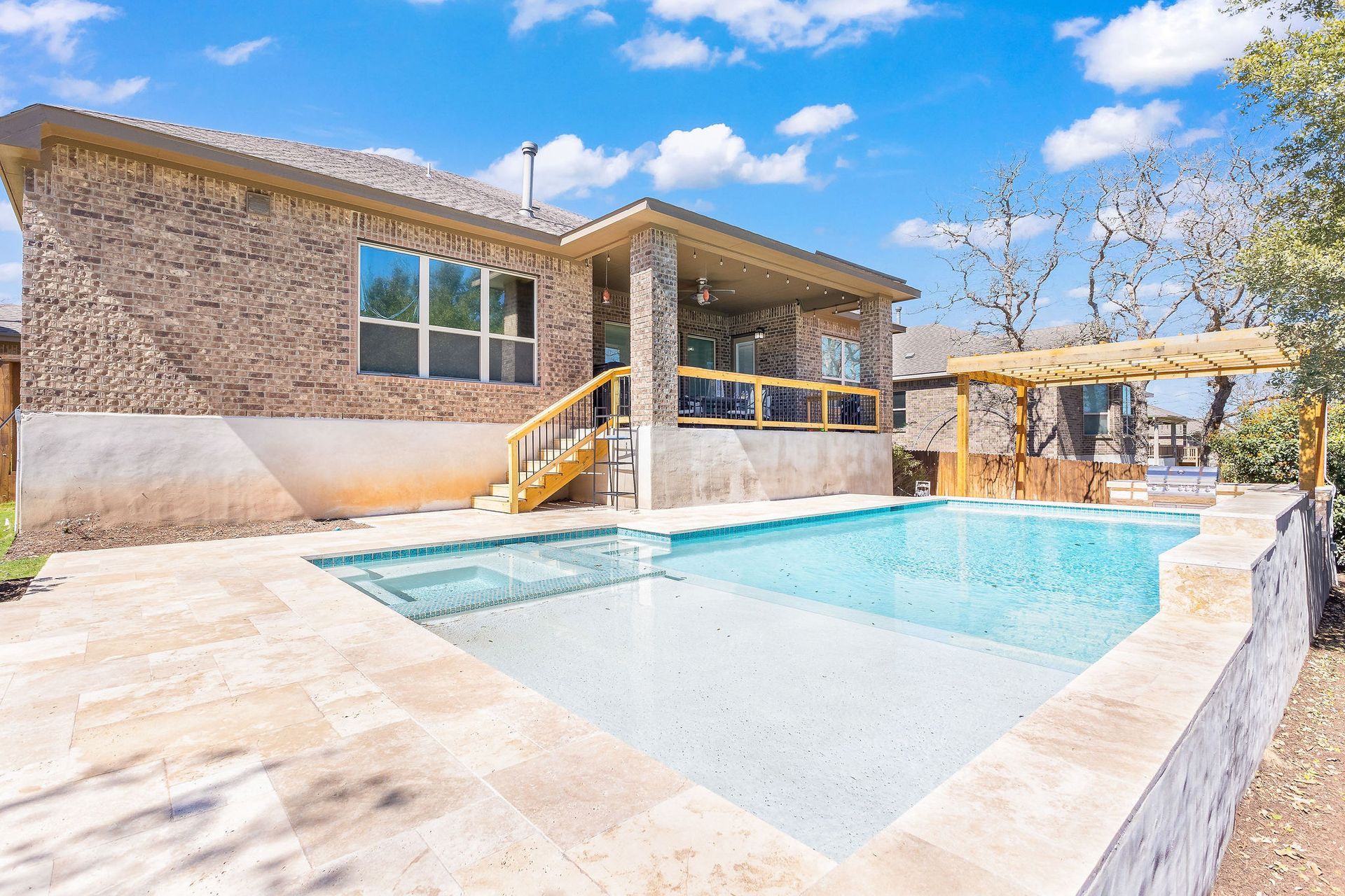 Backyard pool beside a stone house under a bright blue sky