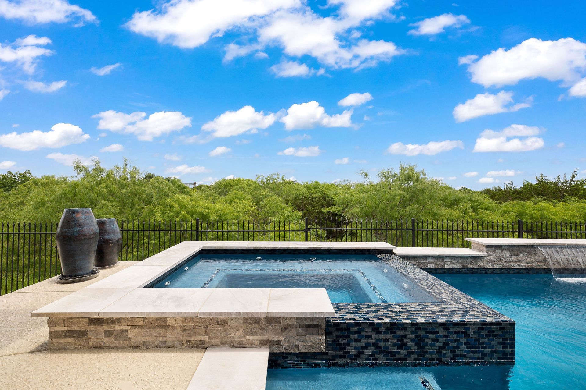Modern outdoor infinity pool with blue water, stone deck, and lush green hedge under a bright sky