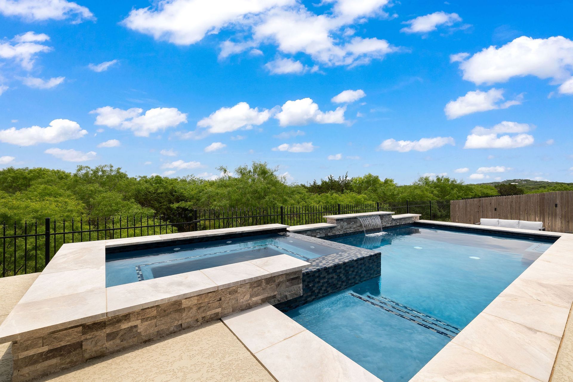 Modern outdoor infinity pool with blue water, stone deck, and lush green hedge under a bright sky