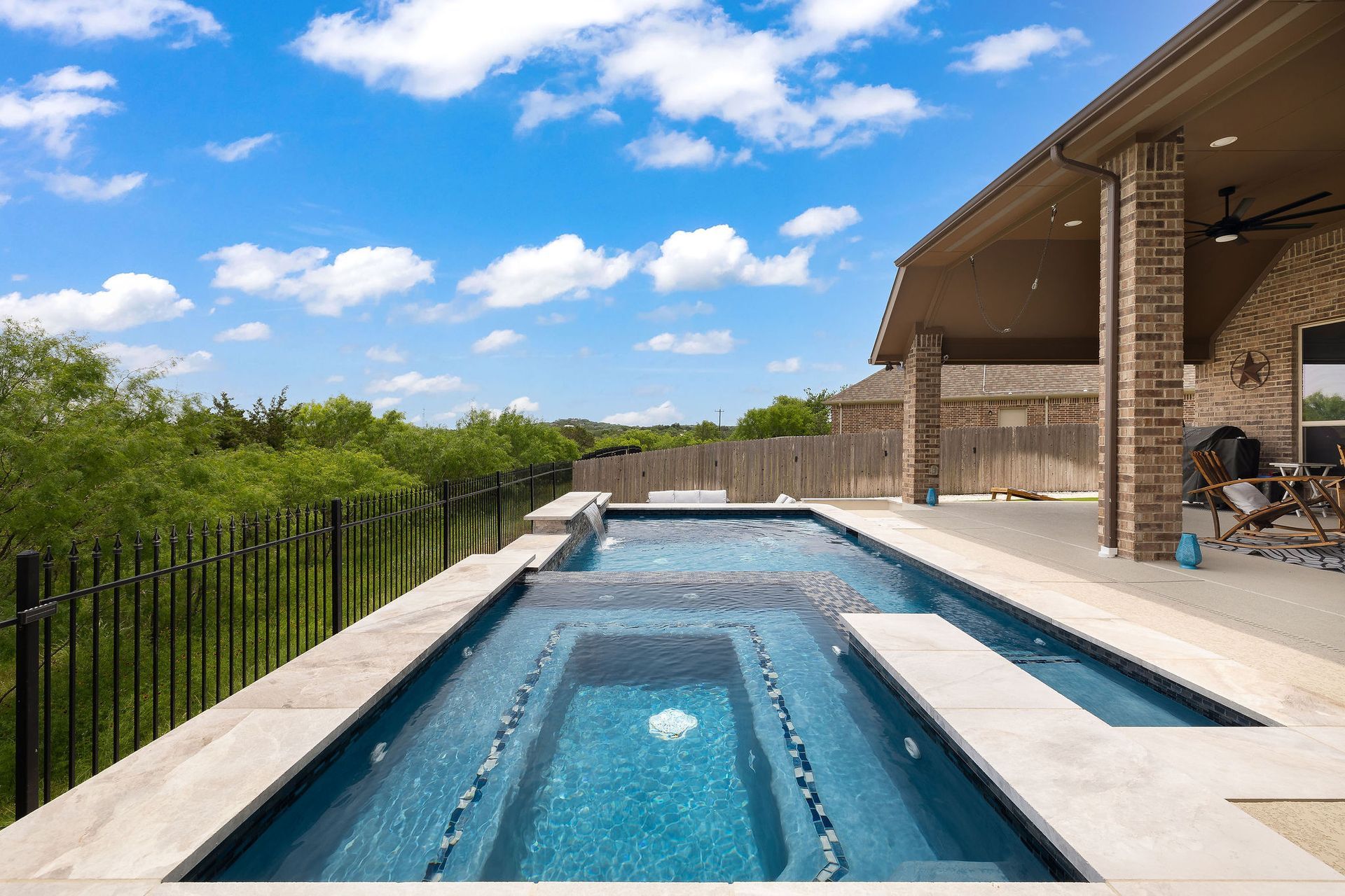 Modern outdoor infinity pool with blue water, stone deck, and lush green hedge under a bright sky