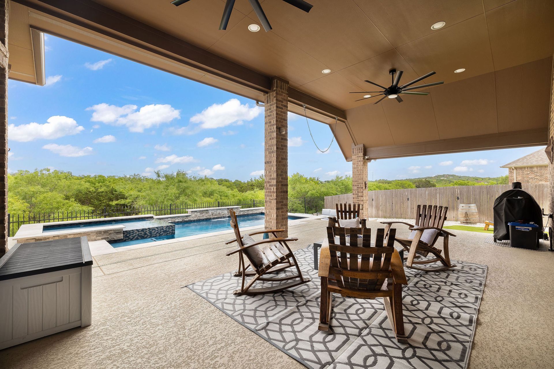 Covered patio with seating overlooking a backyard pool and green landscape