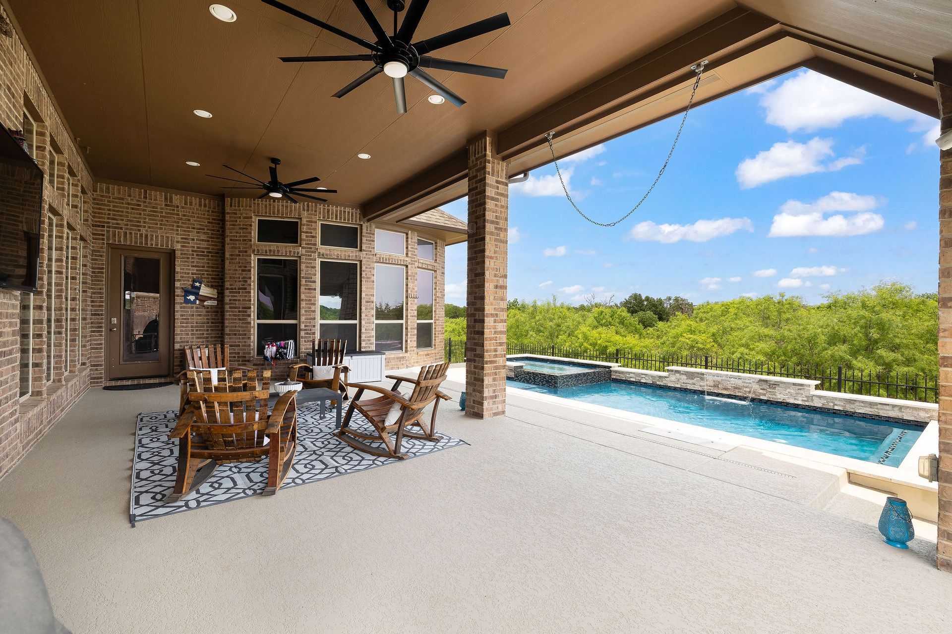 Covered patio with outdoor dining set beside a pool and green landscape beyond