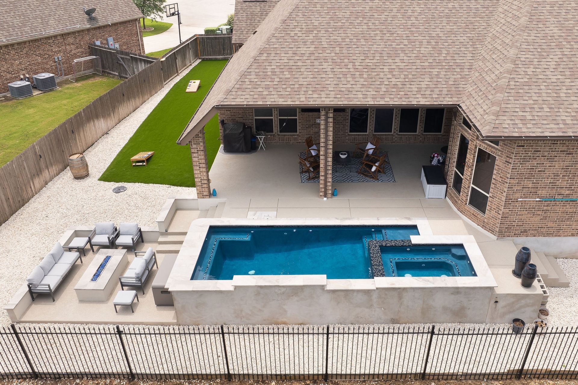 Backyard patio with a rectangular pool, hot tub, and gray outdoor seating beside a brick house