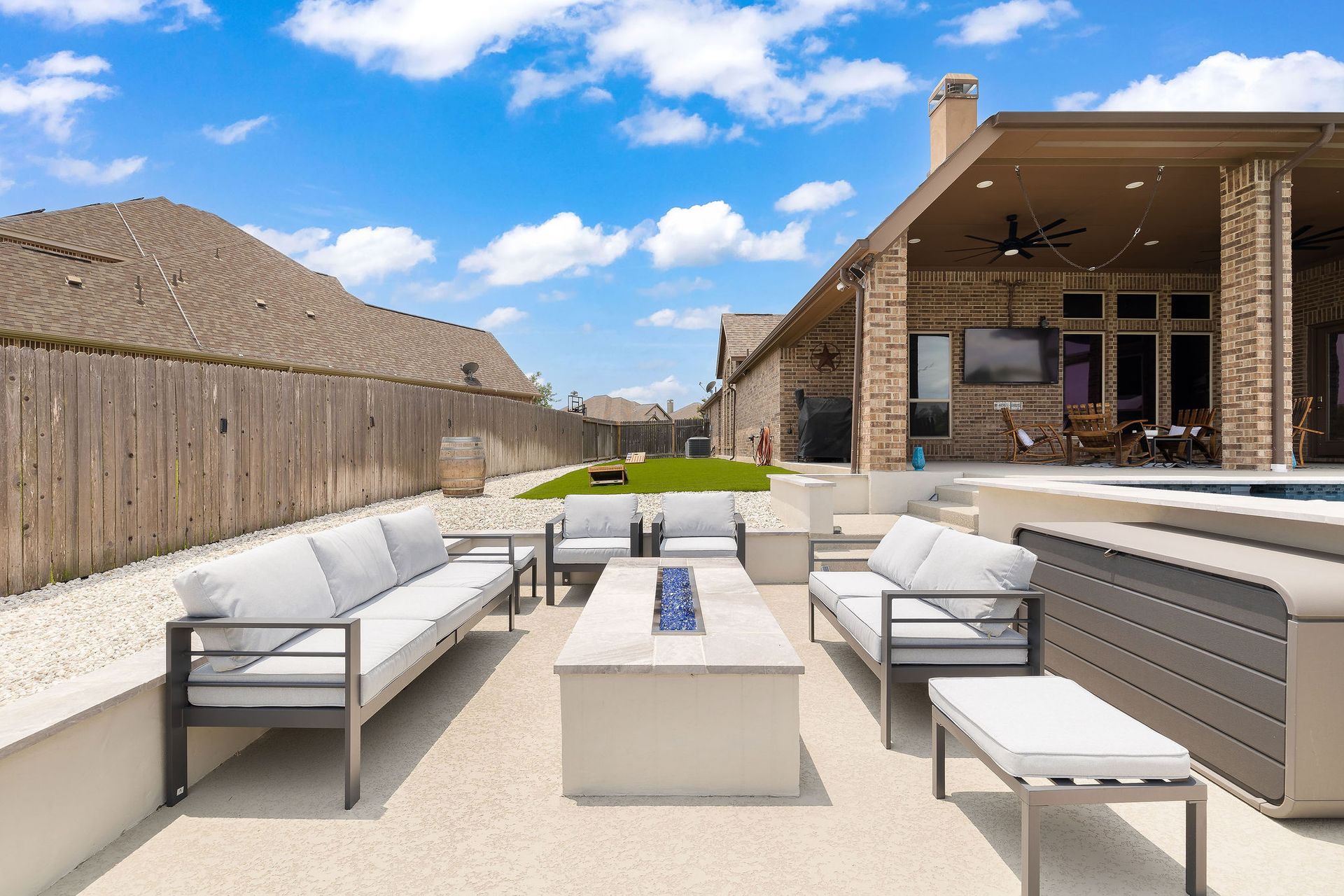 Modern outdoor patio with white seating, fire pit, and covered lounge area under a blue sky
