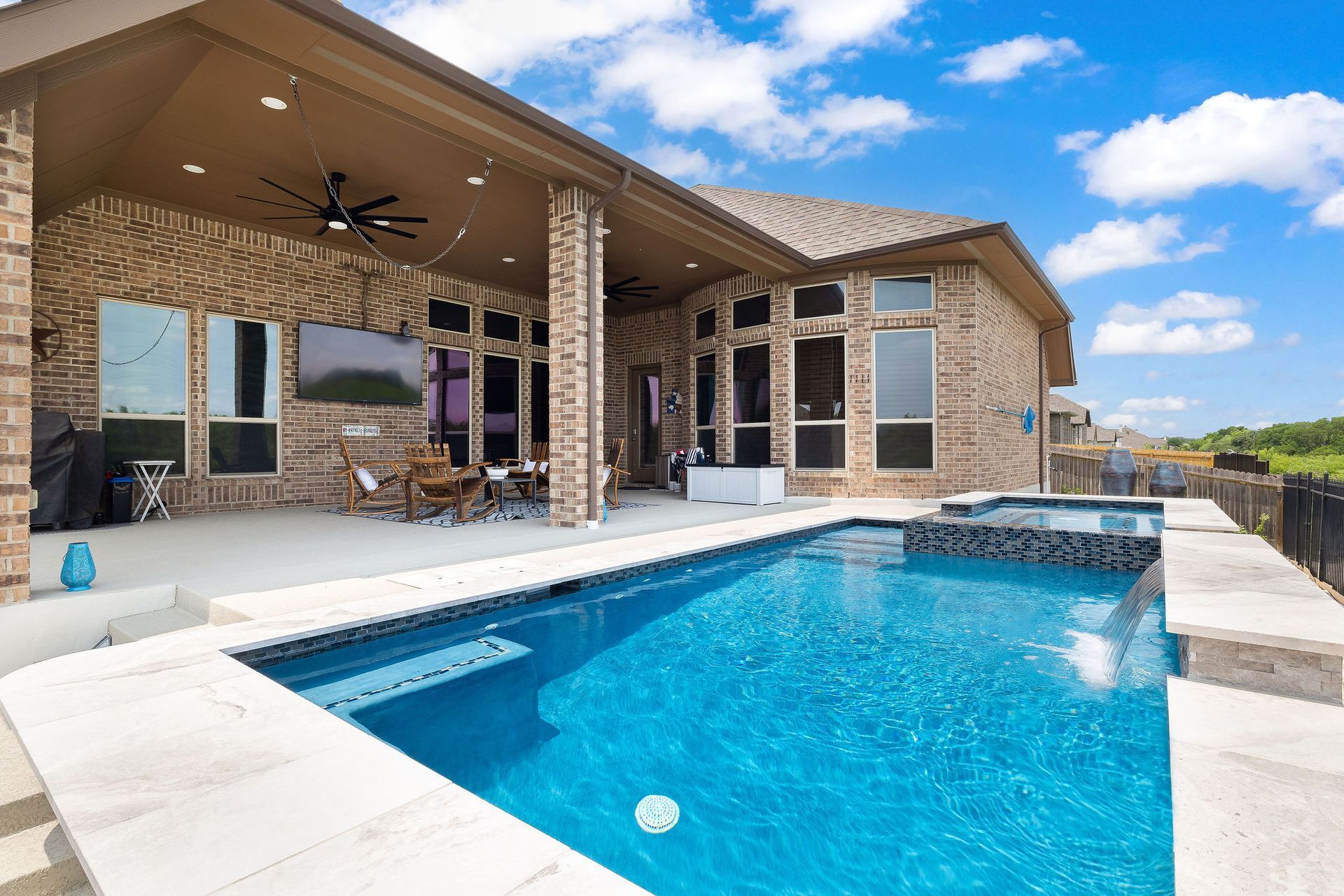 Modern backyard patio with a covered seating area and a rectangular swimming pool under a blue sky