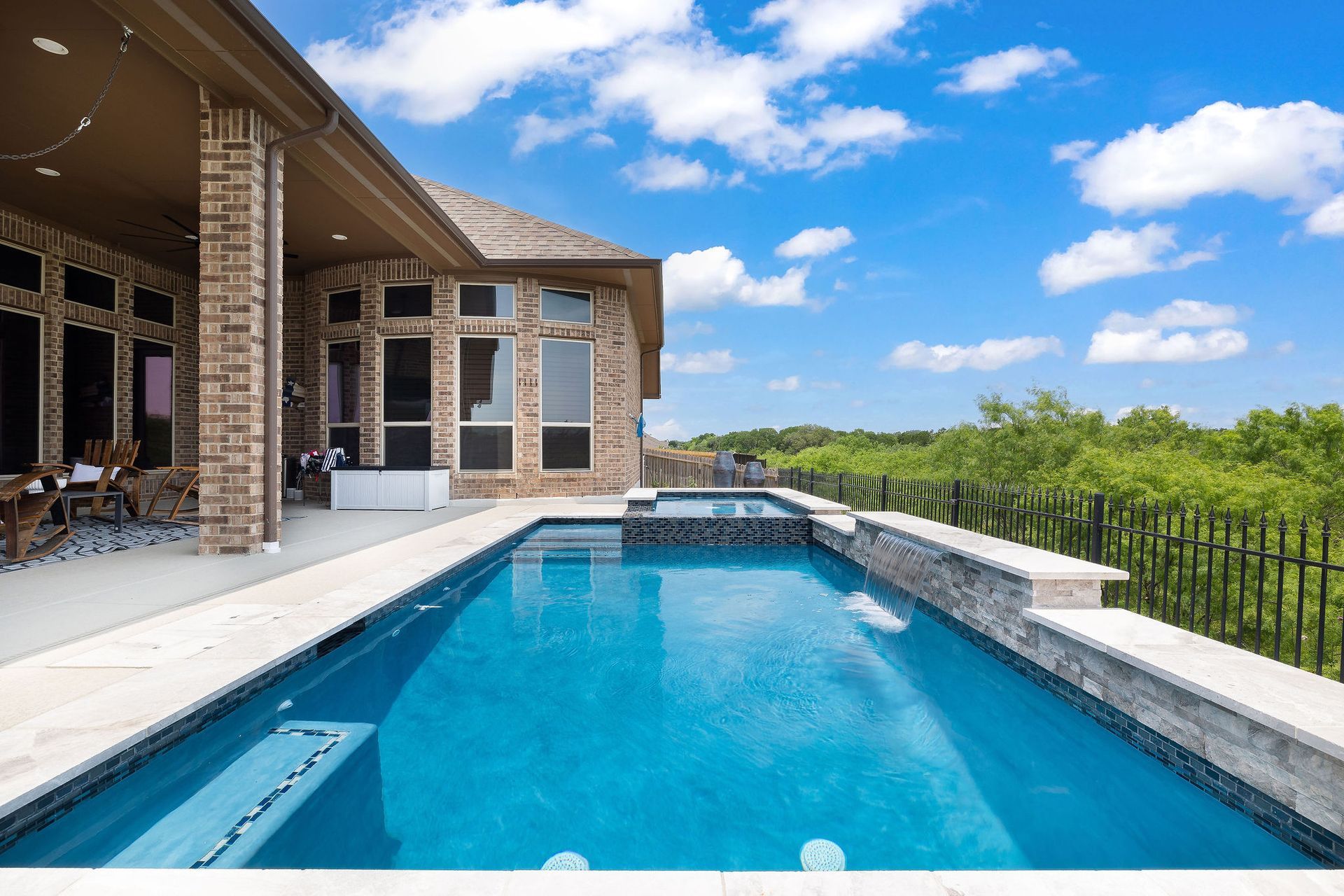 Modern backyard patio with a covered seating area and a rectangular swimming pool under a blue sky