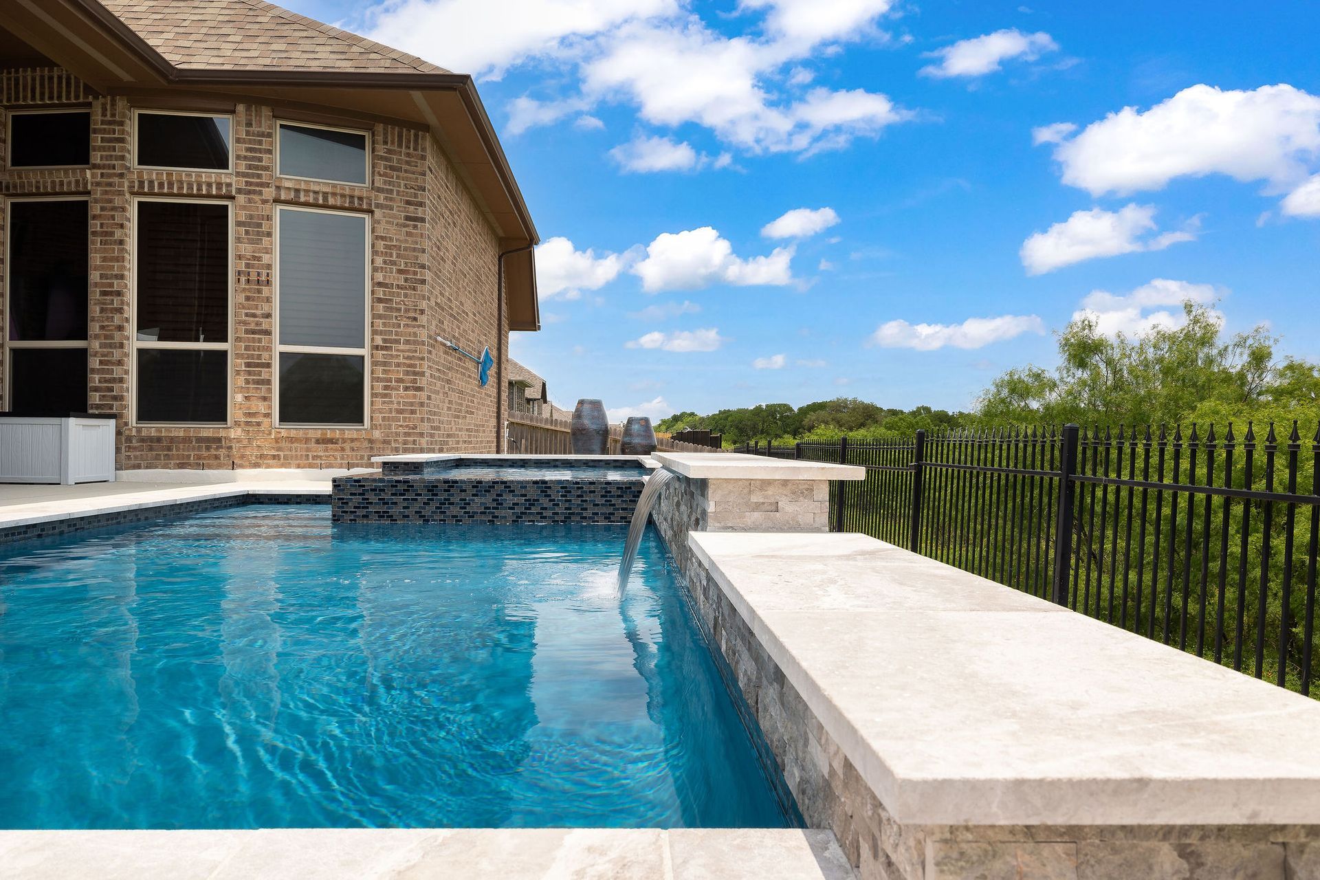 Modern backyard patio with a covered seating area and a rectangular swimming pool under a blue sky