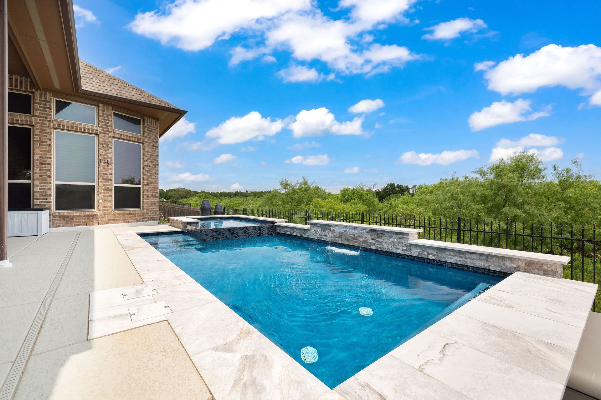 Modern backyard patio with a covered seating area and a rectangular swimming pool under a blue sky