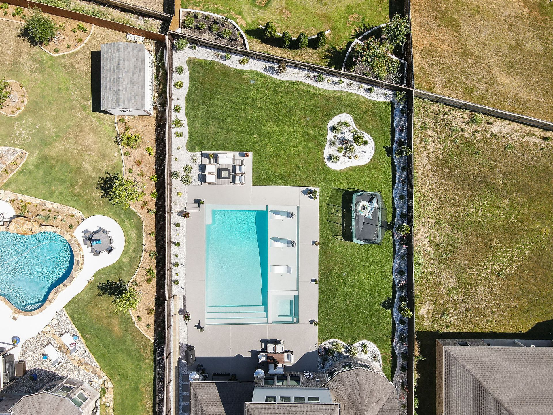 Aerial view of a backyard with a rectangular pool, lawn, patio furniture, and a hot tub.