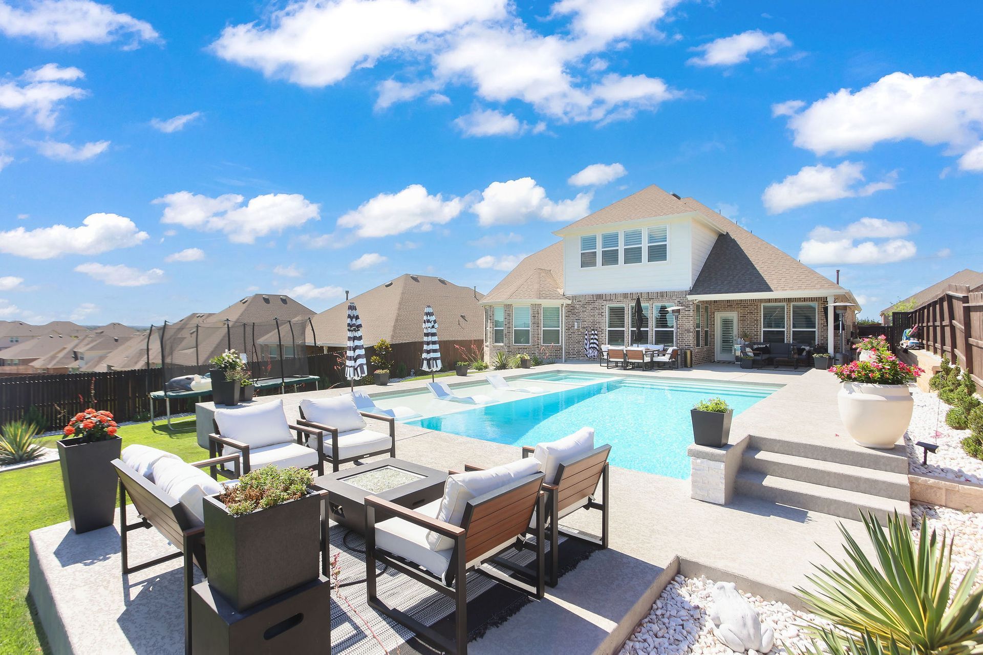 Sunny outdoor swimming pool with lounge chairs and umbrellas in a residential backyard.