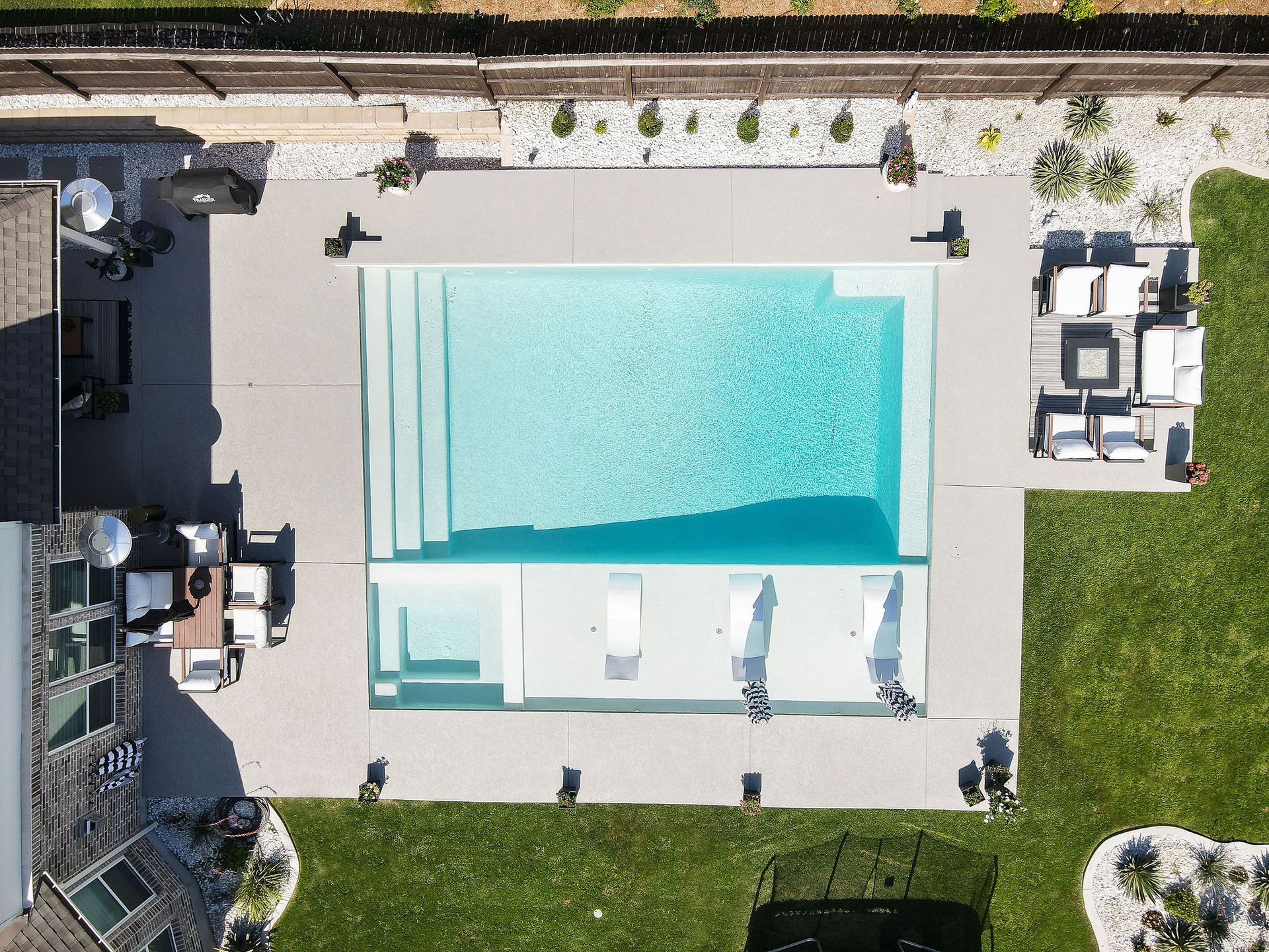 Aerial view of a backyard pool with lounge chairs and a small seating area beside green lawn