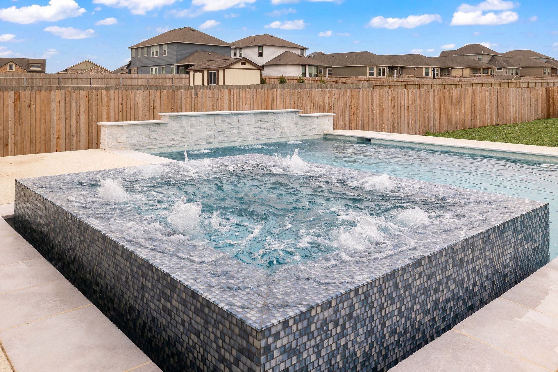 Modern backyard hot tub with bubbling water, stone tile exterior, and a wooden privacy fence behind it