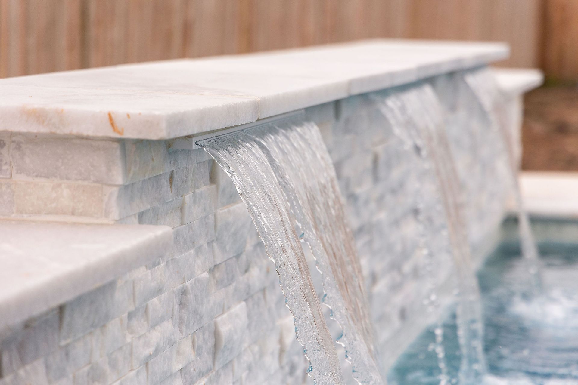 Stone waterfall spilling into a pool beside a tiled ledge