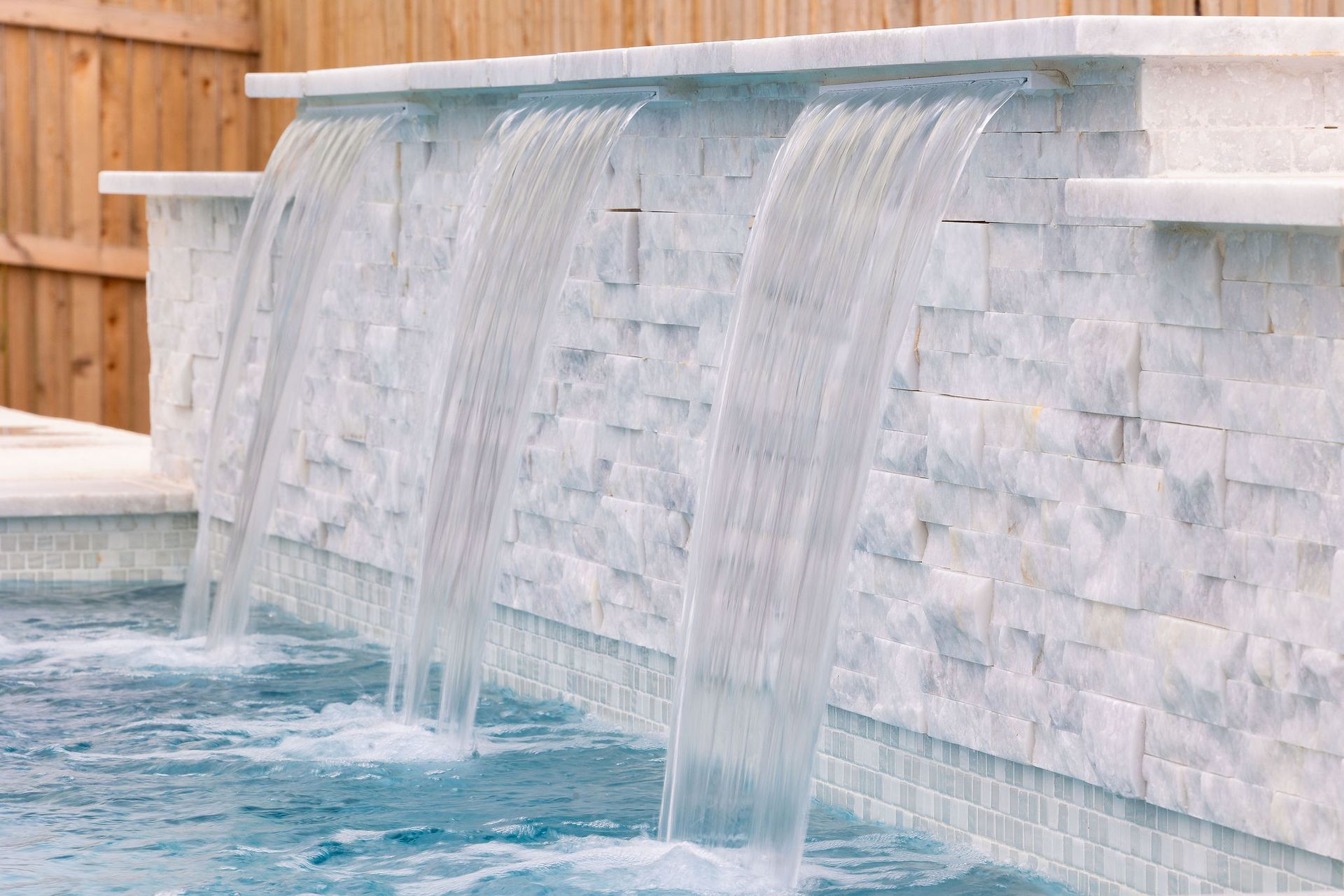 White stone waterfall spilling into a blue pool beside a wooden fence