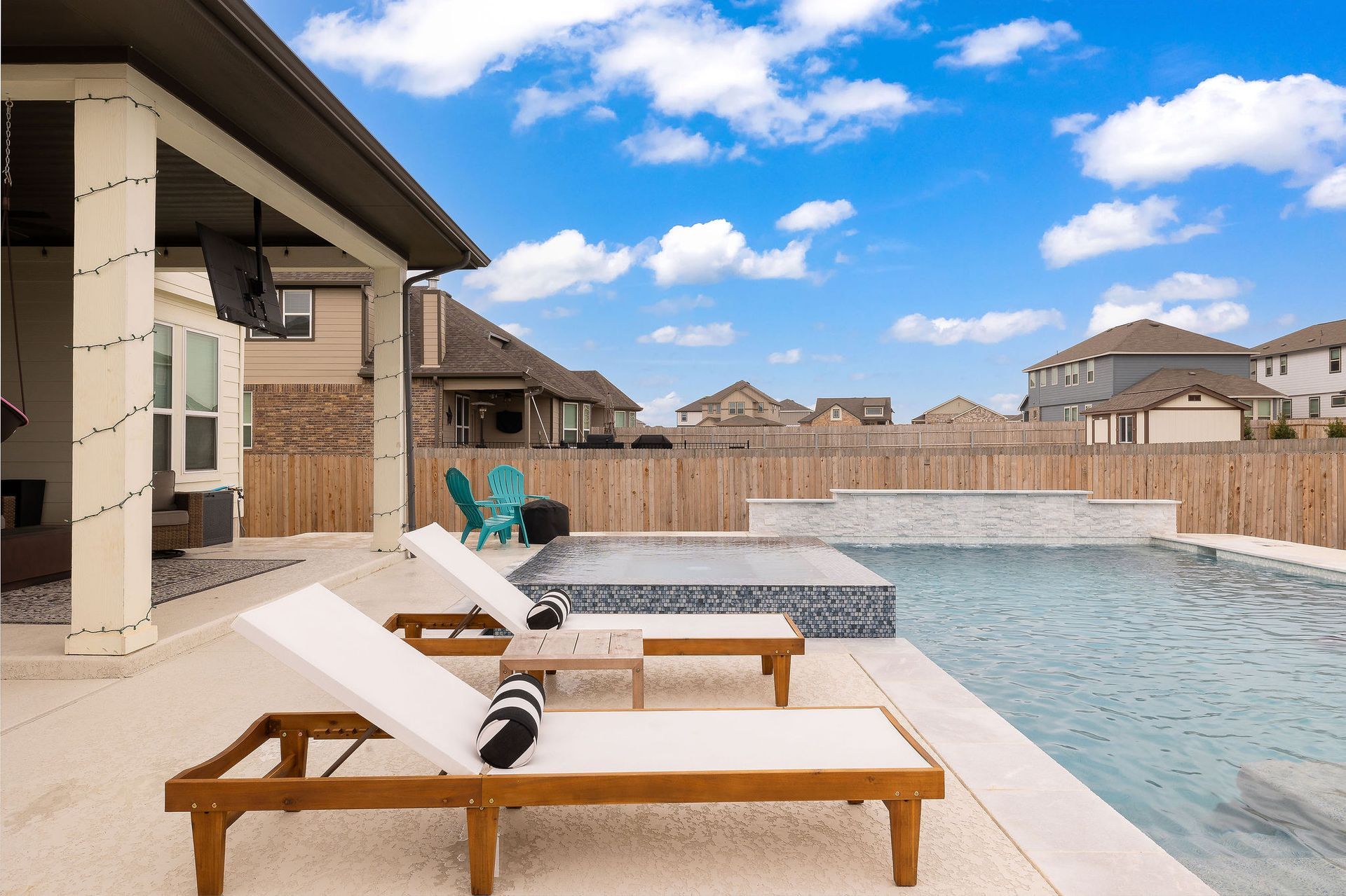 Poolside lounge chairs beside a backyard swimming pool under a blue sky