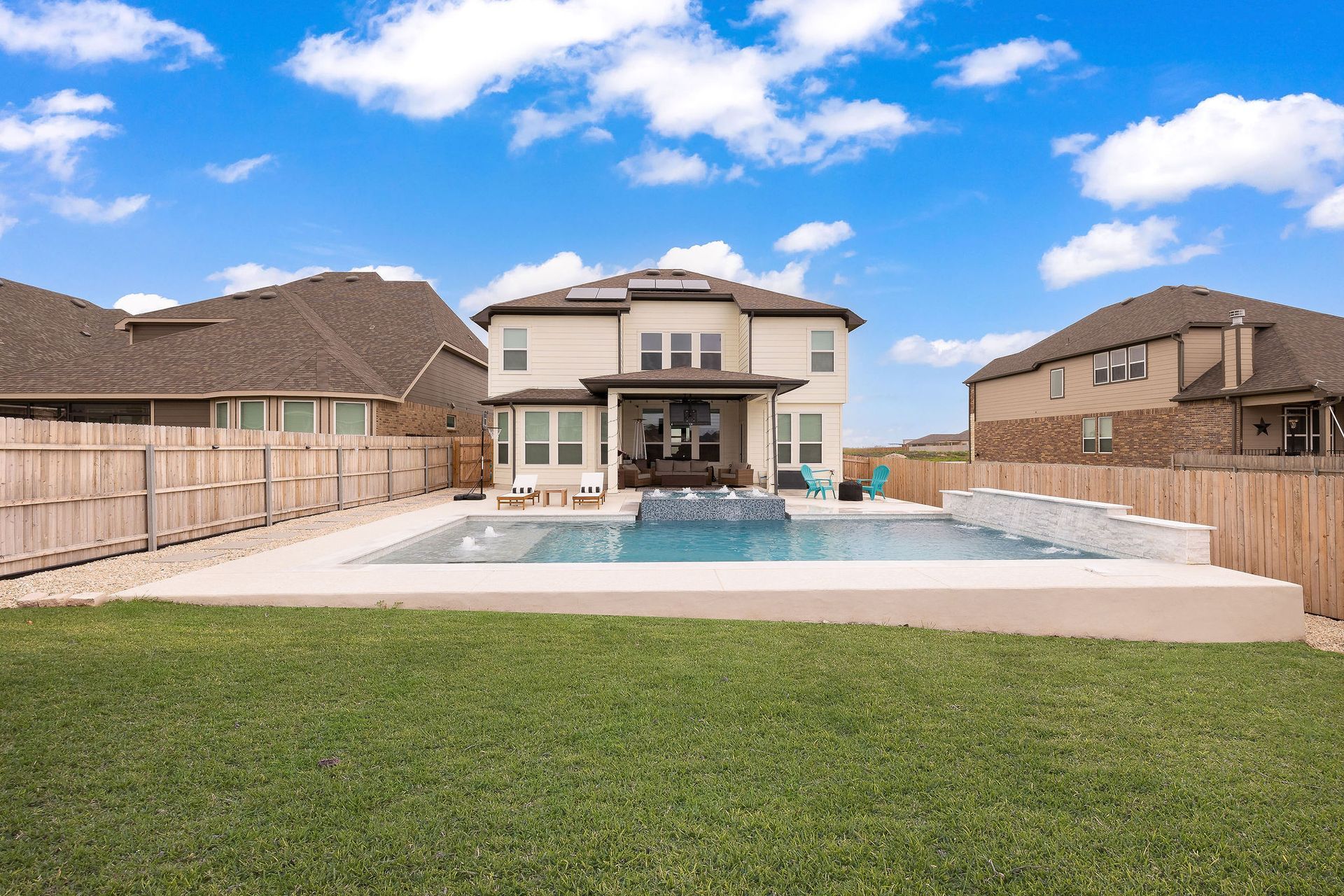 Backyard patio with a modern two-story house and a large swimming pool under a blue sky