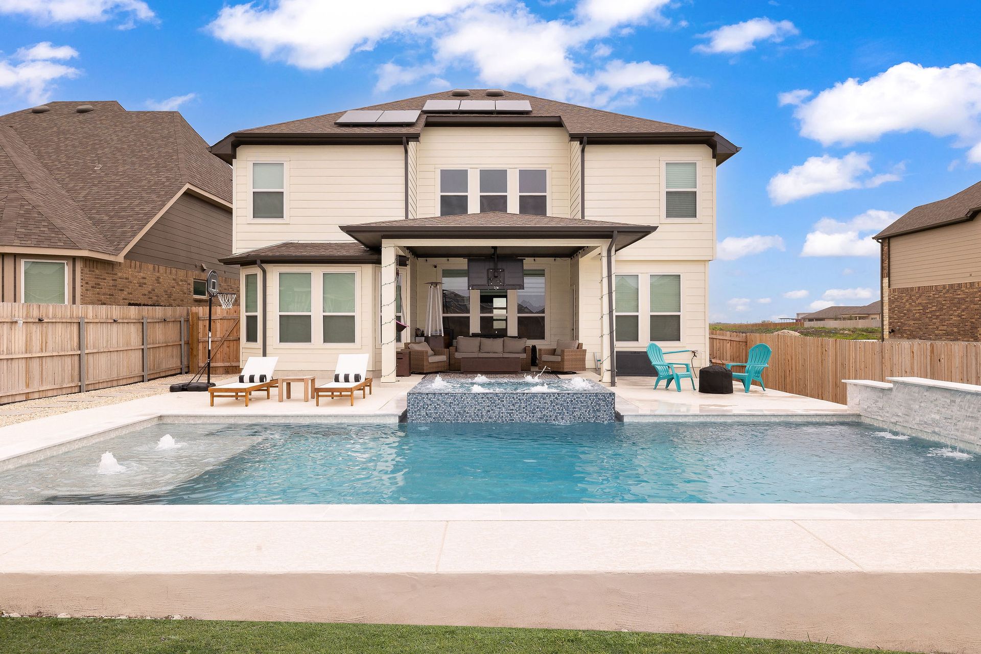 Backyard with a two-story house, patio, and swimming pool under a blue sky
