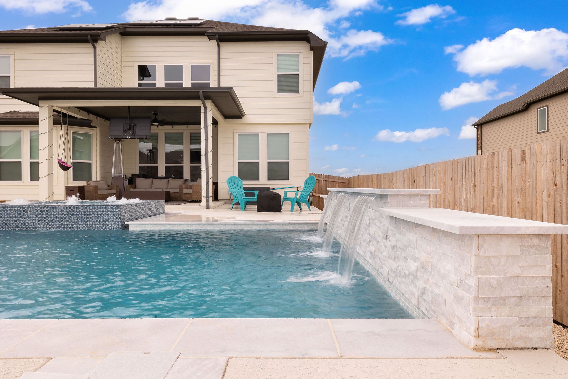 Backyard pool with a covered patio, lounge chairs, and a two-story house behind it