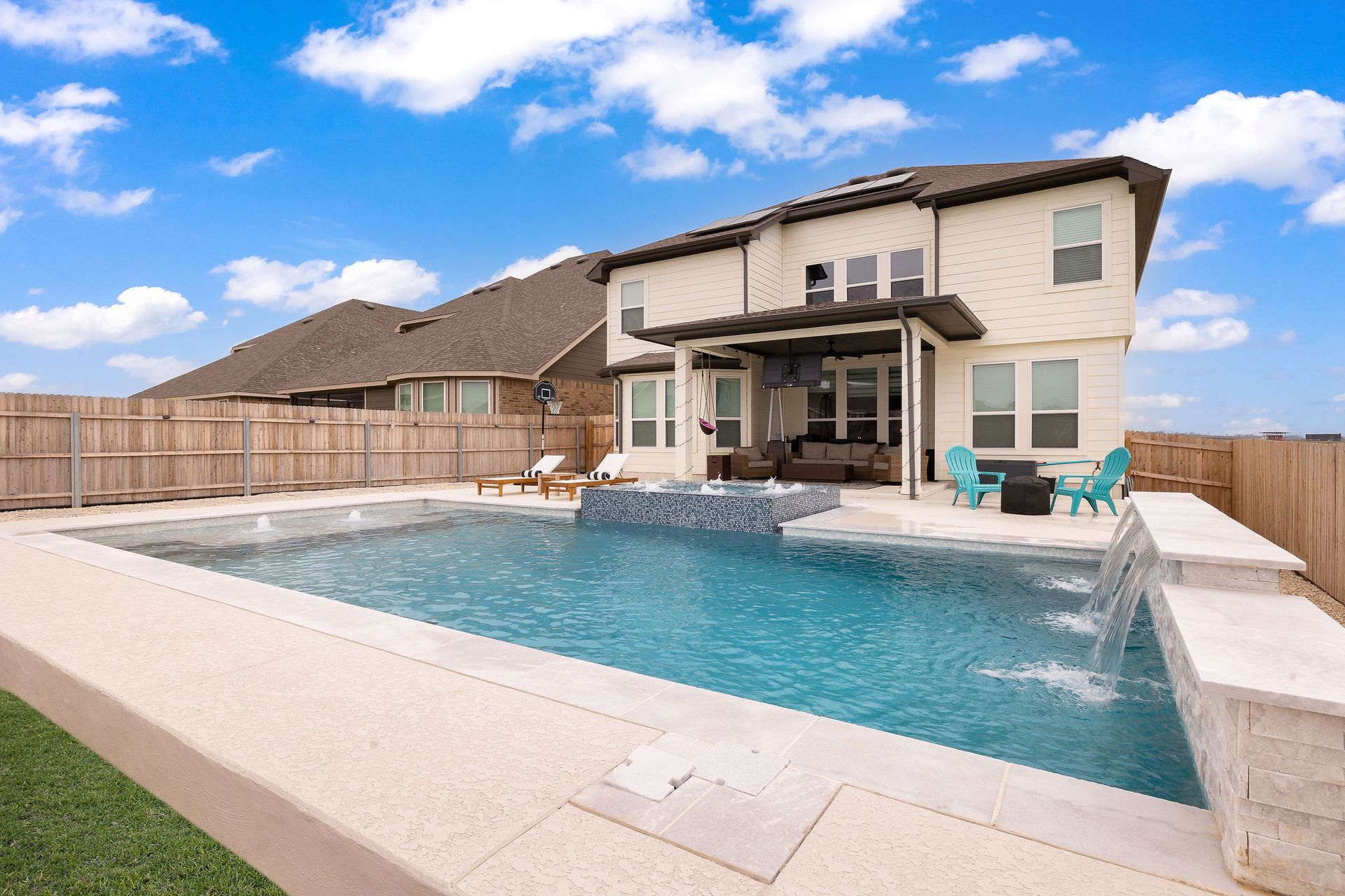 Backyard pool with a covered patio, lounge chairs, and a two-story house behind it