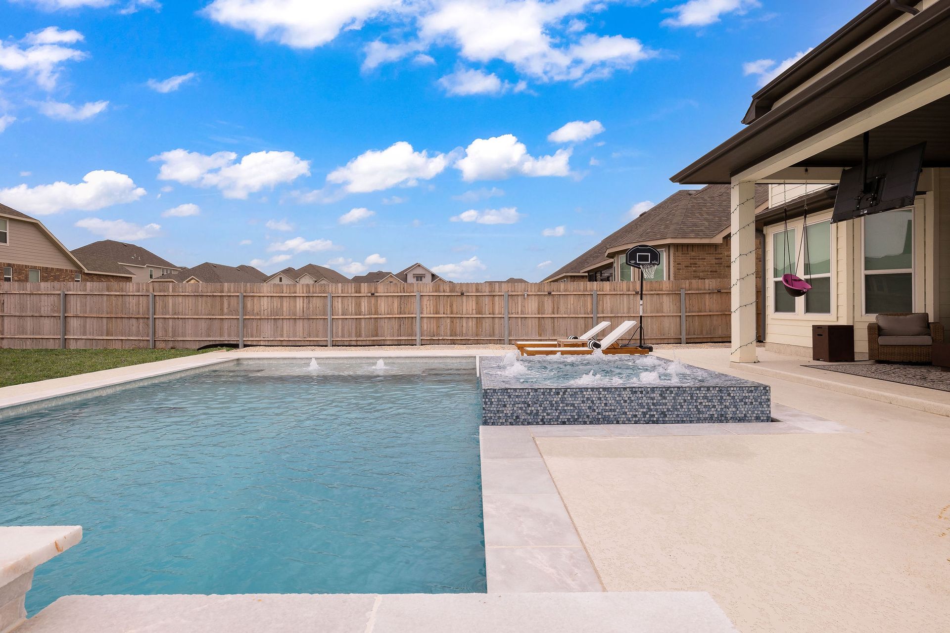 Backyard pool with a covered patio, lounge chairs, and a two-story house behind it