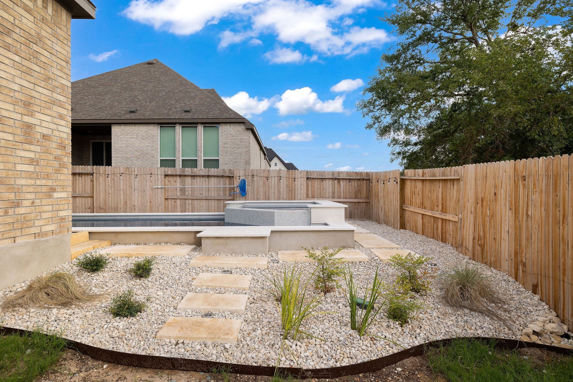 Backyard patio with stone path, raised seating area, gravel beds, and wooden privacy fence beside a house
