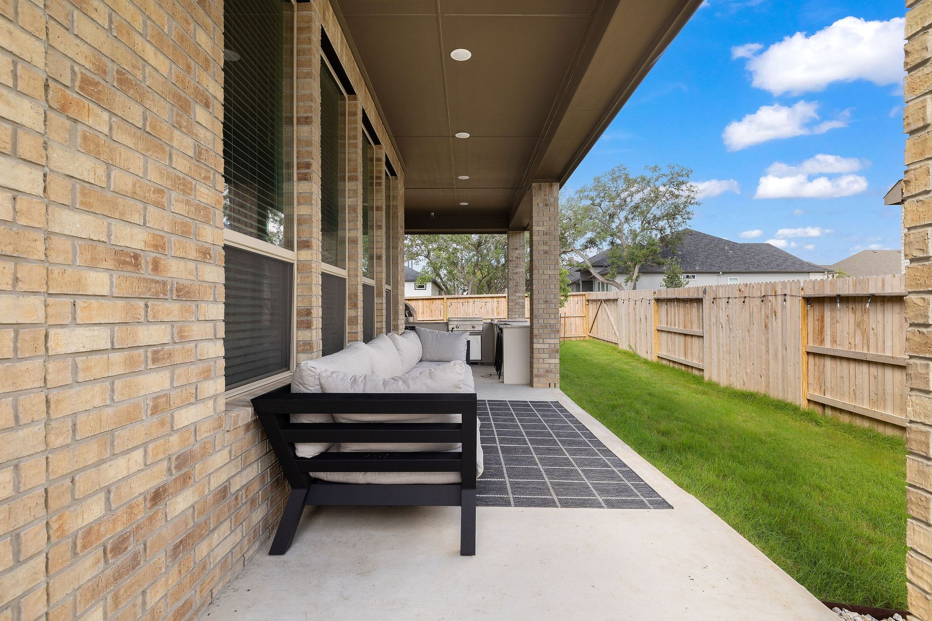 Covered patio with black bench, brick wall, tiled floor, and green lawn beside a wooden fence