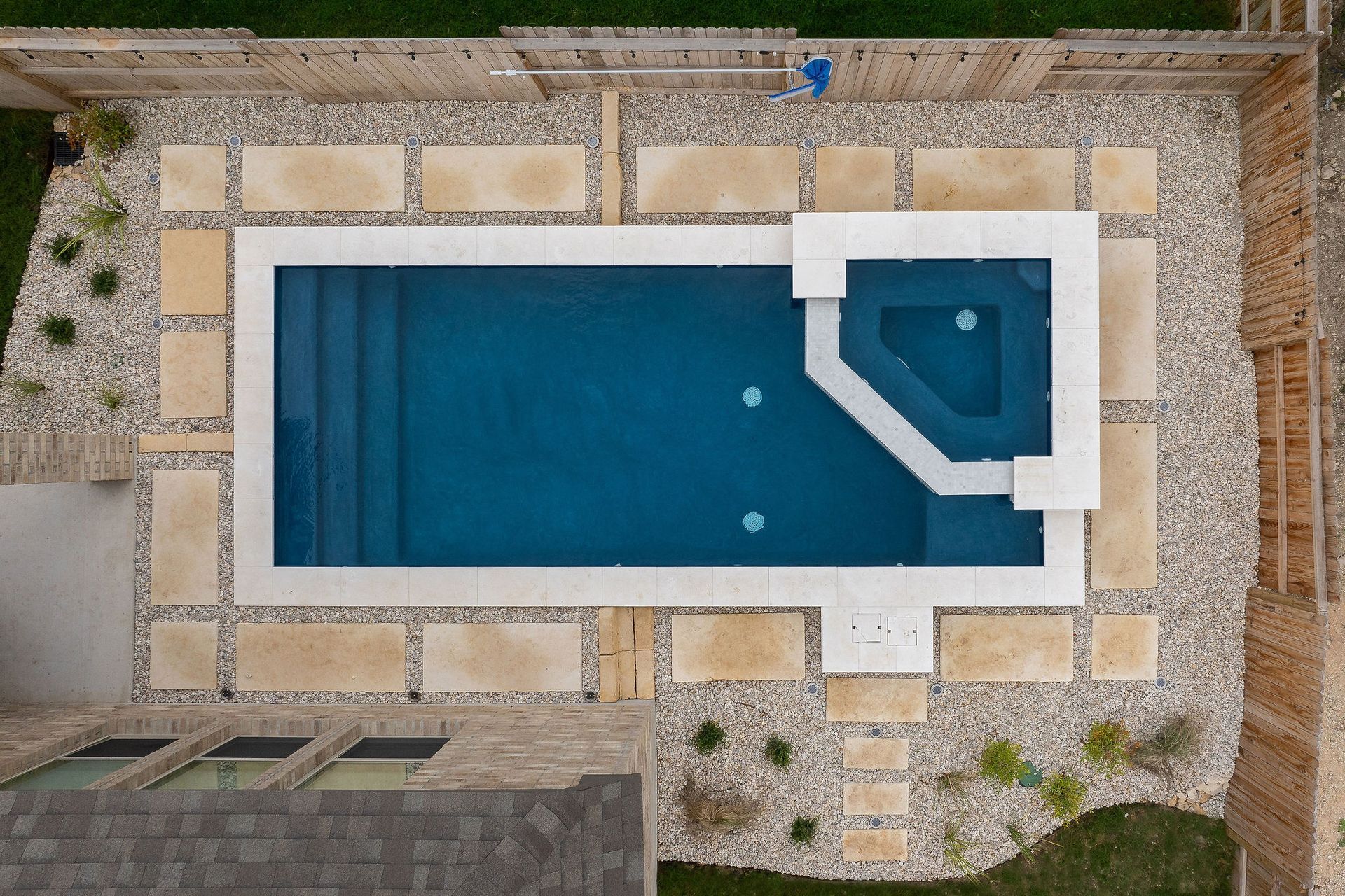 Top-down view of a rectangular blue swimming pool with a small attached spa and stone patio surround