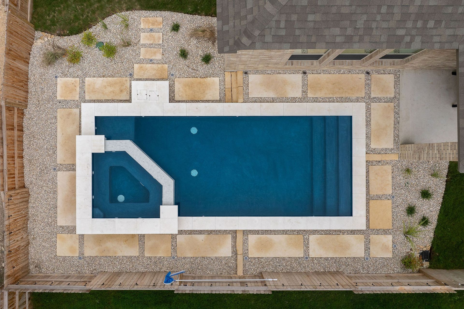 Top-down view of a rectangular blue swimming pool with a smaller attached spa and tan stone patio