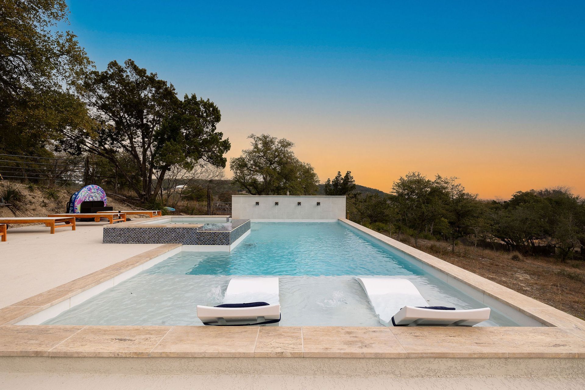 Modern outdoor pool with lounge chairs, sunset sky, and trees in the background