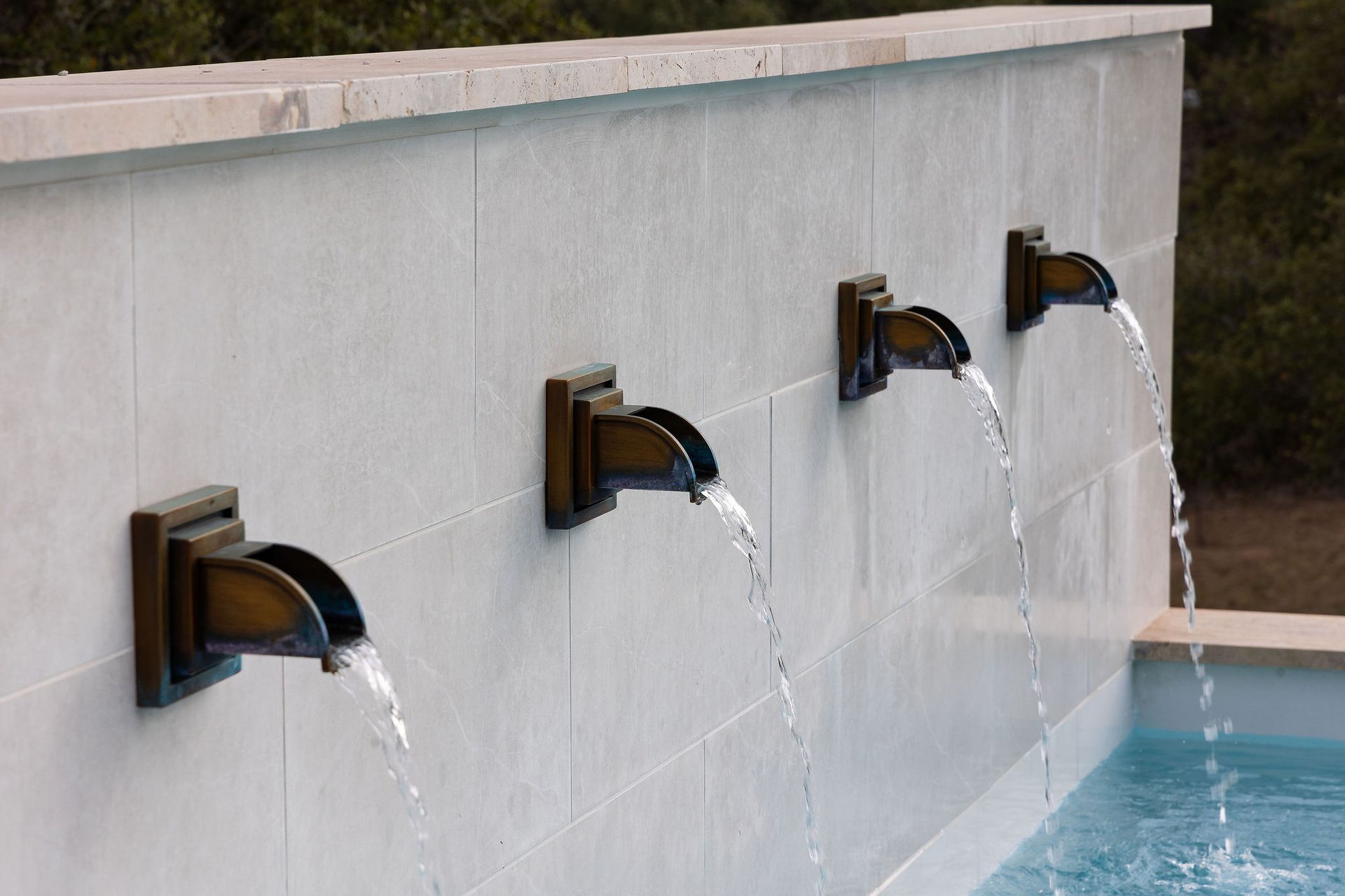 Three bronze wall fountains pouring water into a blue pool