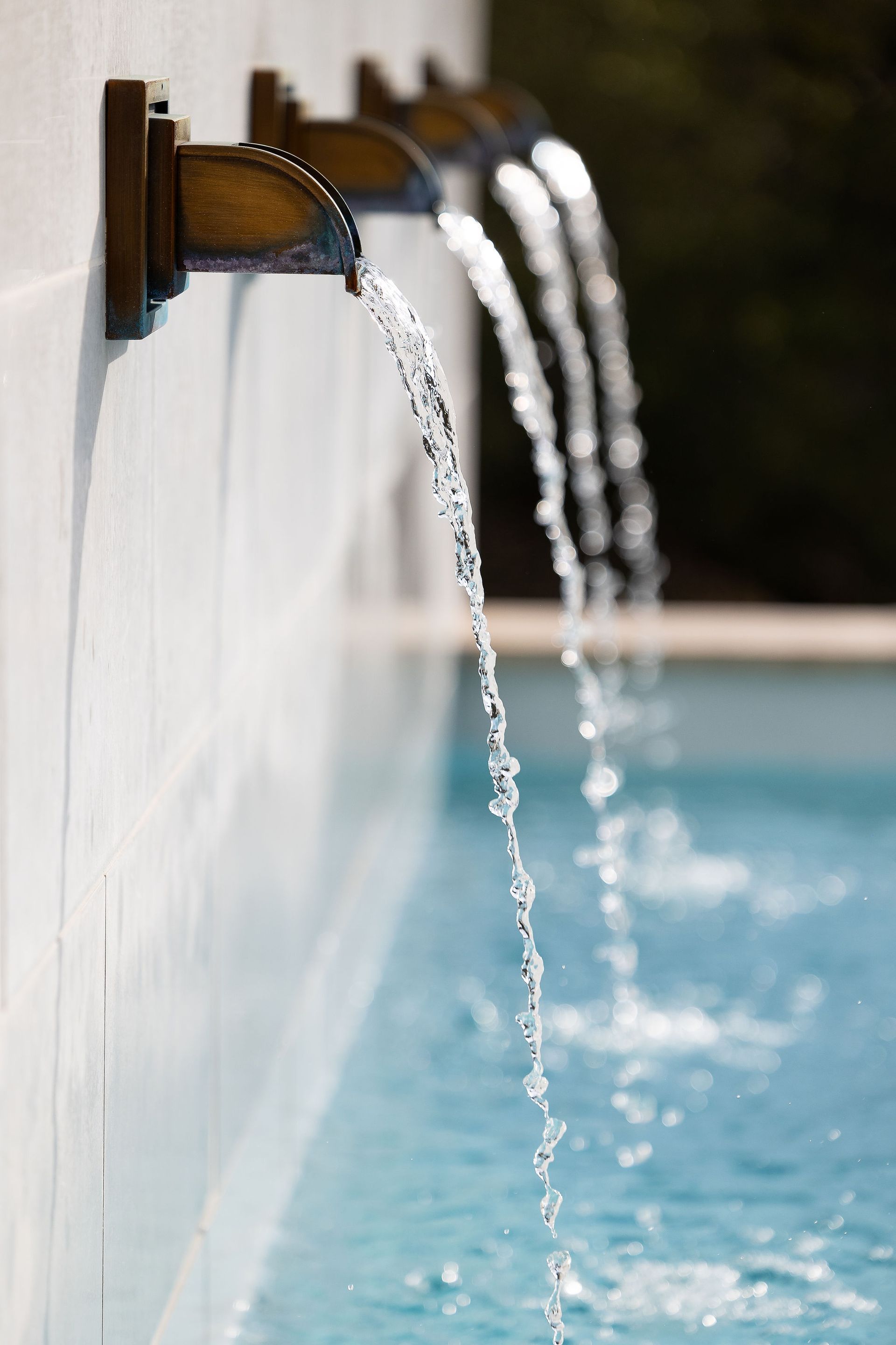 Wall-mounted pool fountains pouring water into a blue swimming pool