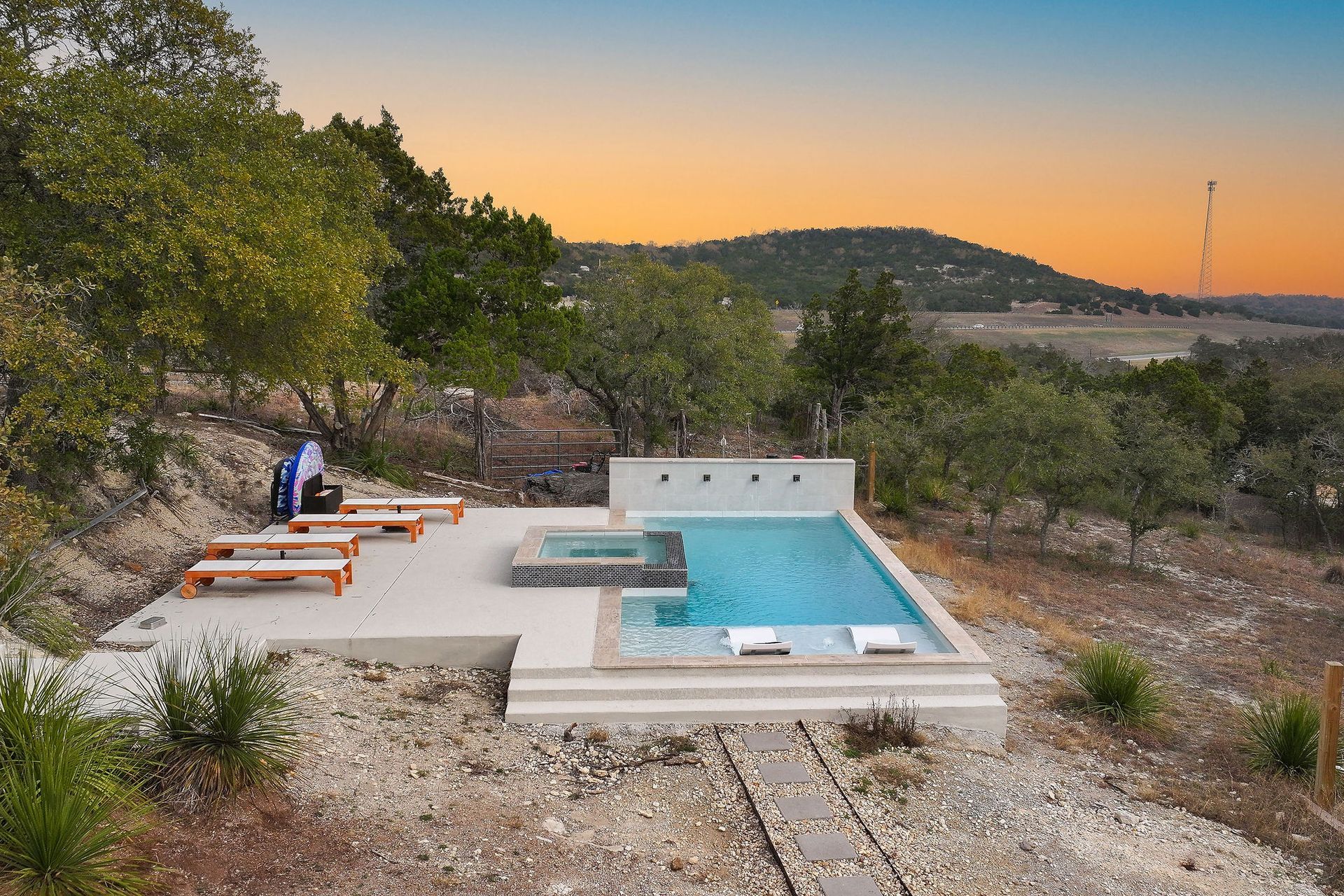 Modern backyard pool with lounge chairs, trees, and a sunset sky