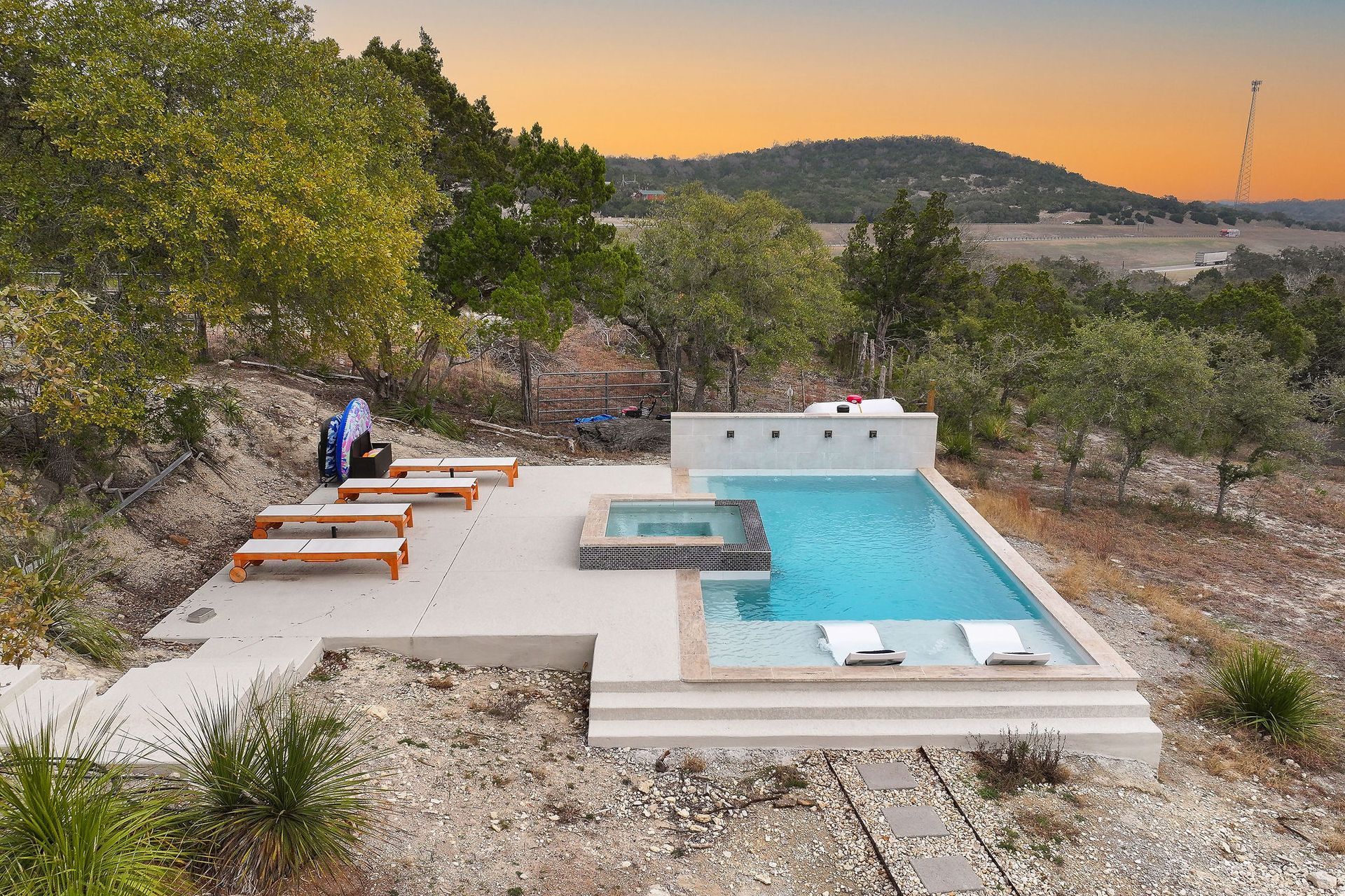 ModModern backyard with a turquoise pool, lounge chairs, trees, and a sunset sky over hills.ern backyard with a turquoise pool, lounge chairs, trees, and a sunset sky over hills.