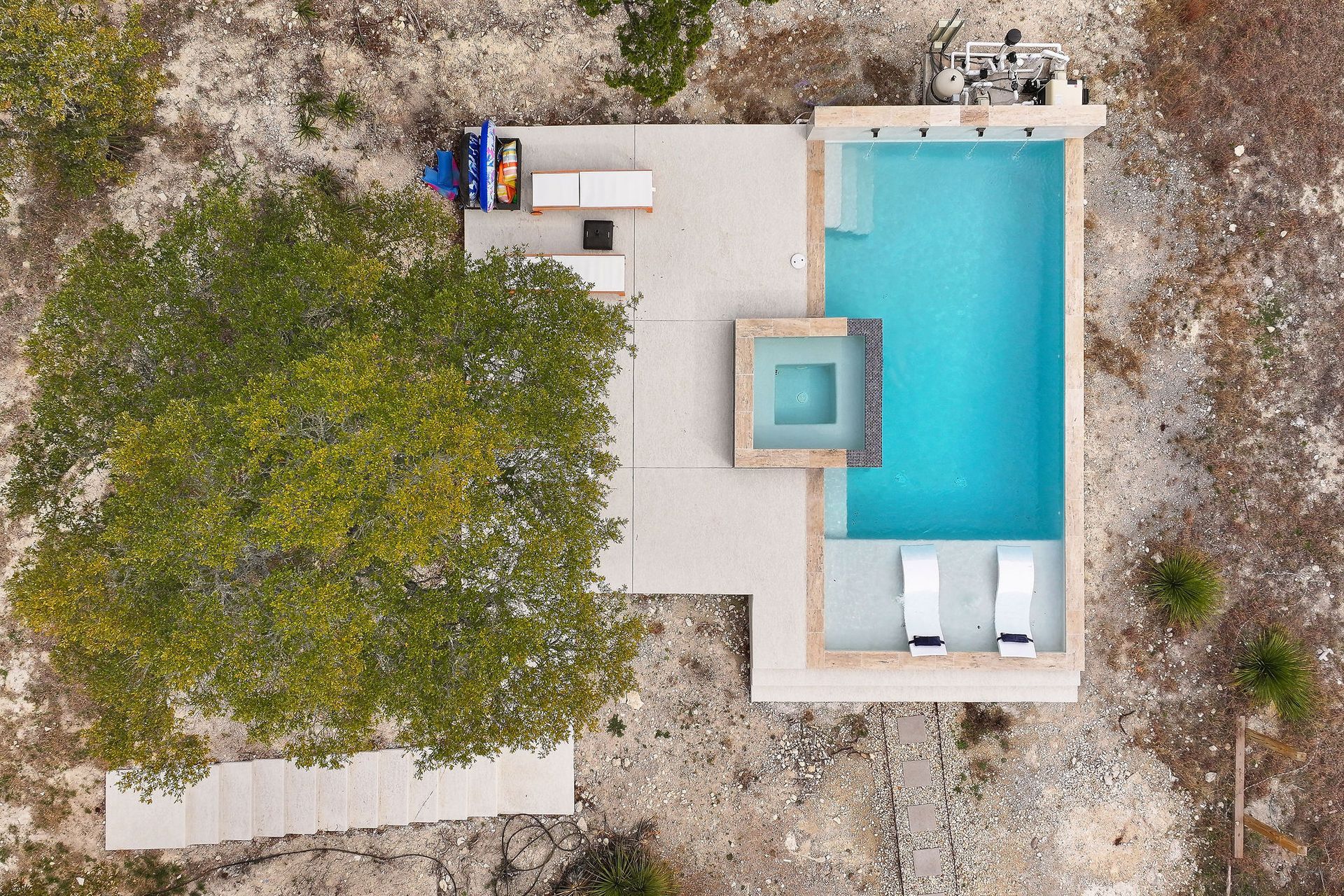 Modern backyard with a turquoise pool, lounge chairs, trees, and a sunset sky over hills.
