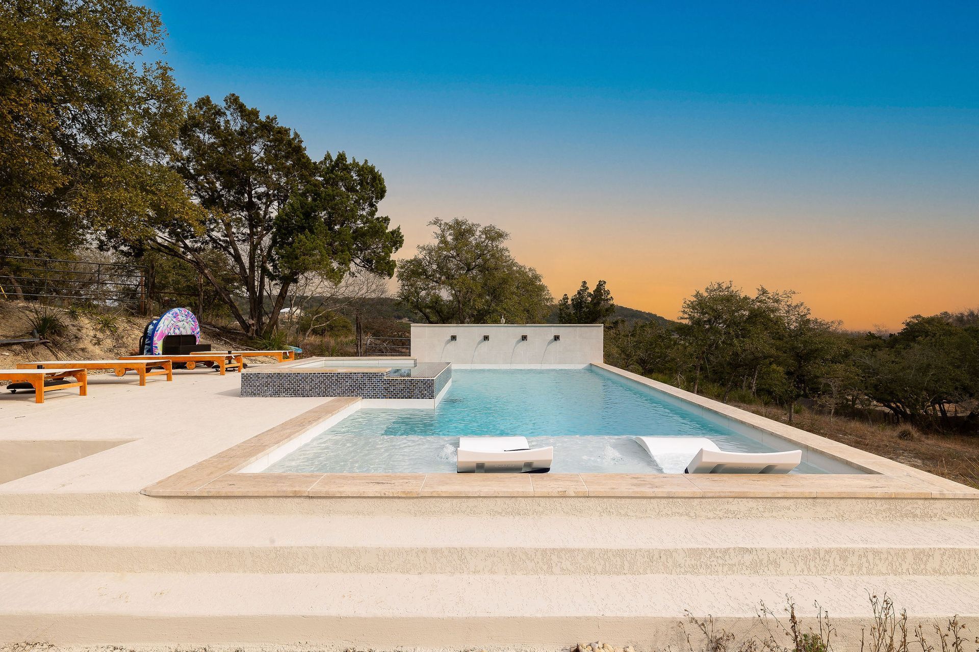 Modern backyard pool with lounge chairs, trees, and a sunset sky