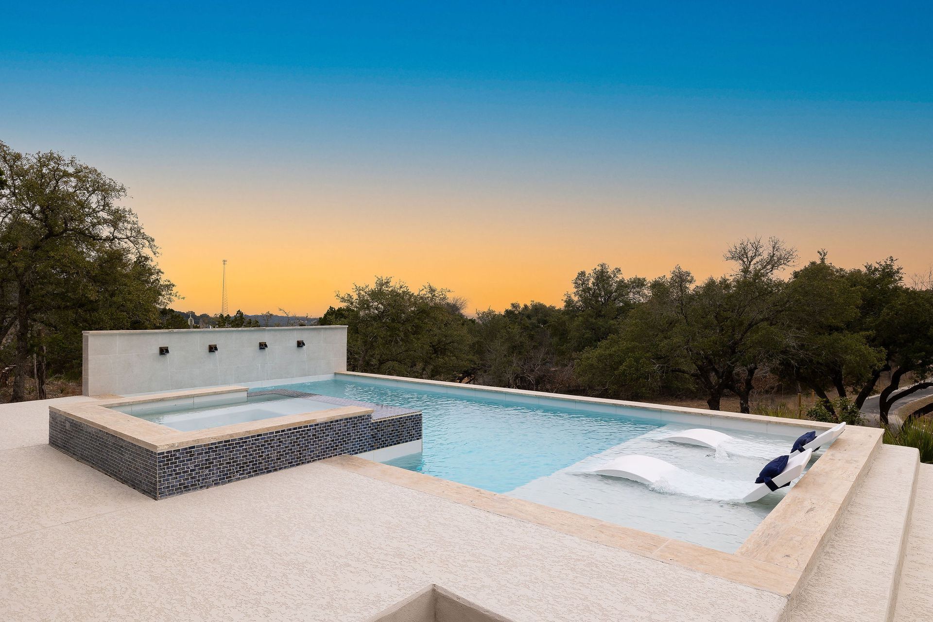 Modern rooftop pool at sunset with lounge chairs and trees in the background