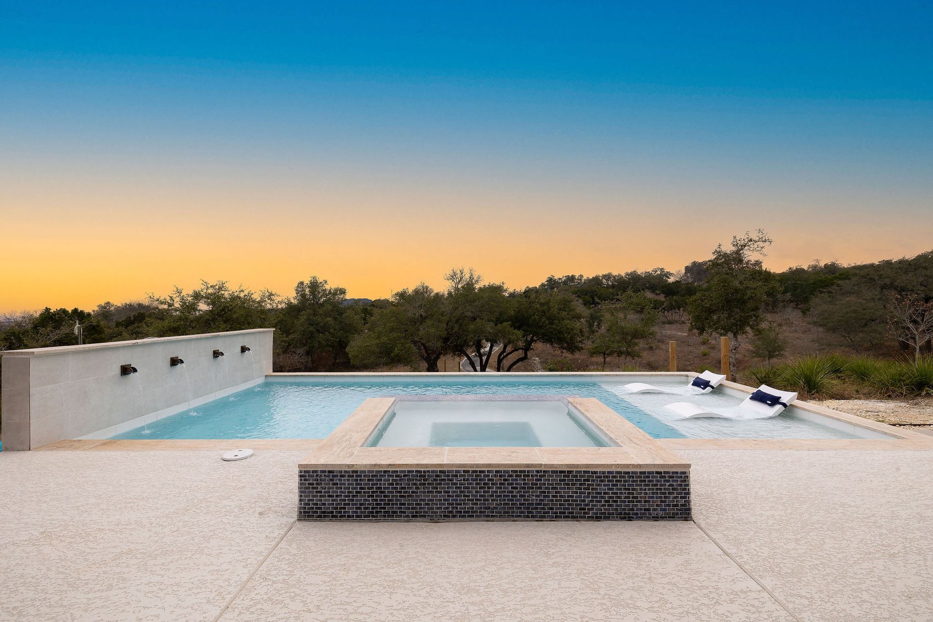 Modern backyard pool with lounge chairs, trees, and a sunset sky