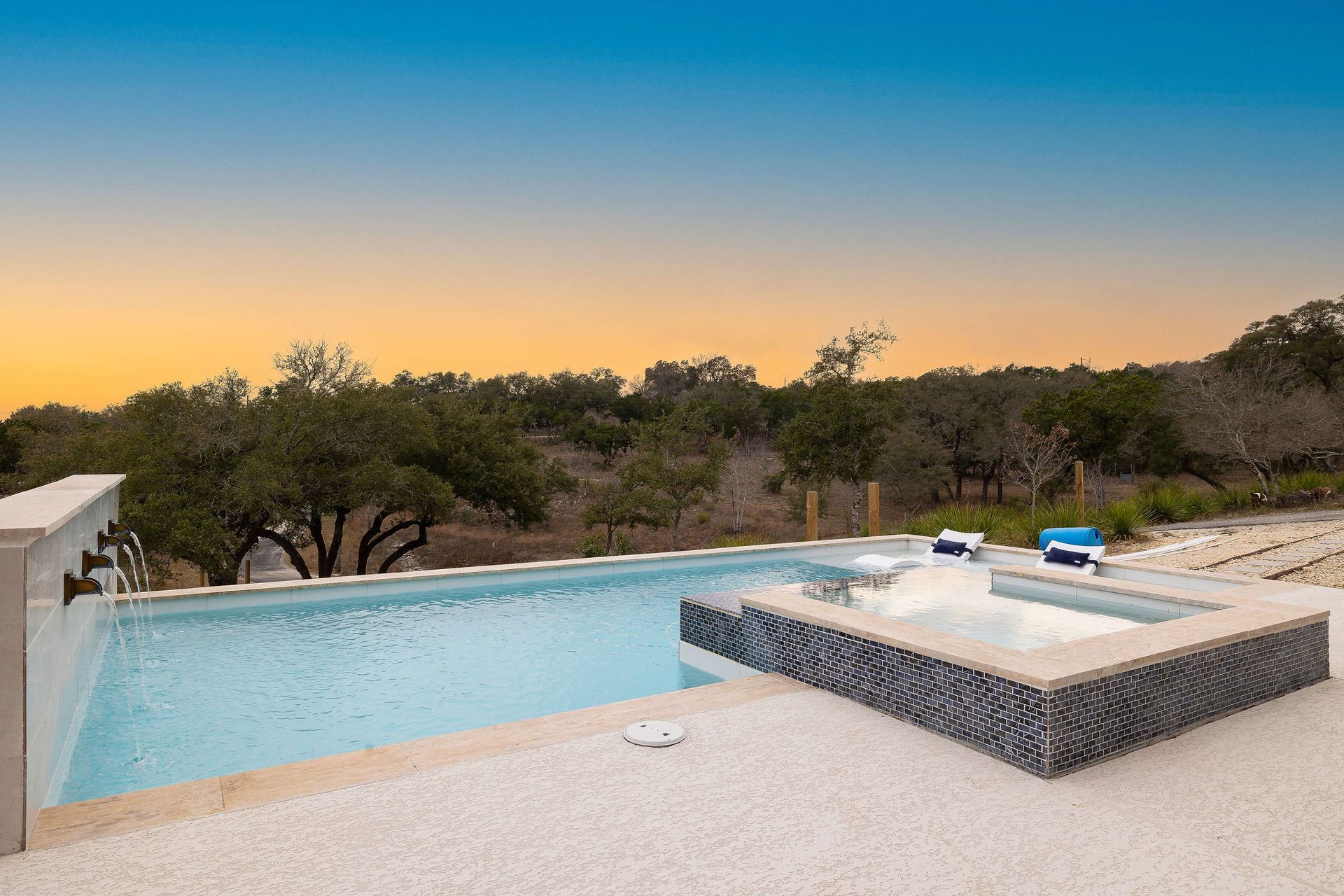 Modern backyard with a turquoise pool, lounge chairs, trees, and a sunset sky over hills.Modern backyard with a turquoise pool, lounge chairs, trees, and a sunset sky over hills.