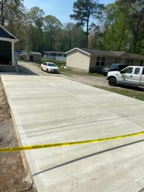 Fresh concrete driveway beside apartment buildings, with caution tape across the foreground and parked cars nearby