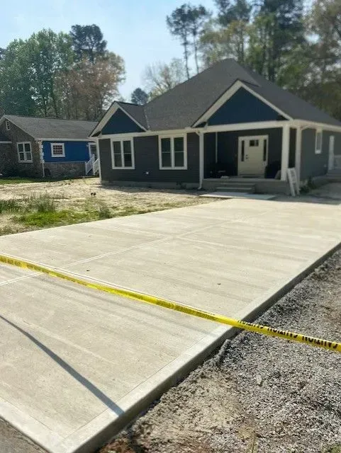 Concrete driveway in front of a dark gray house with white trim and a yellow caution tape across the foreground