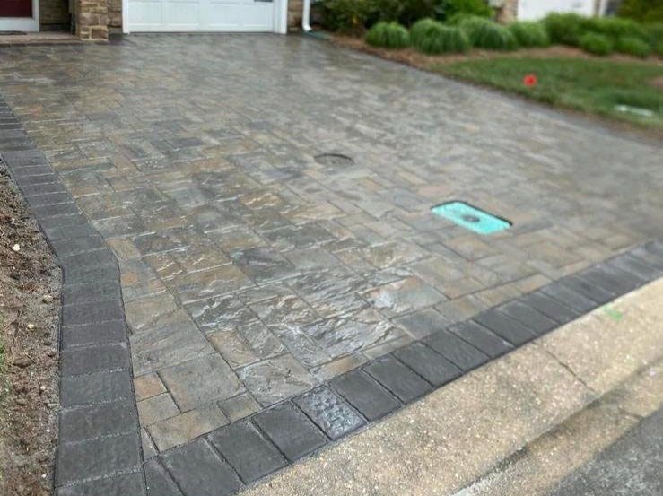 Stone-paved driveway with dark border bricks leading to a garage and house entrance