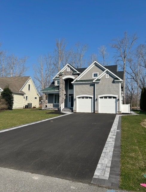 Suburban house with a two-car garage and freshly paved driveway under a clear blue sky