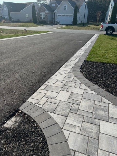 Curved stone paver sidewalk meeting a residential street corner beside a grassy lawn.