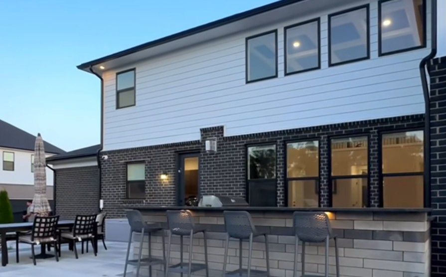 A modern two-story home exterior with white horizontal siding and dark brick, featuring a patio bar and outdoor seating.