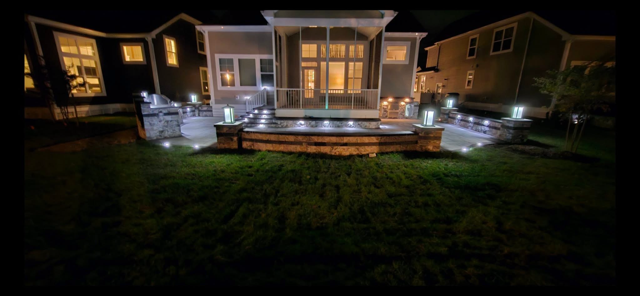 Lit backyard deck at night with string lights and a patio seating area