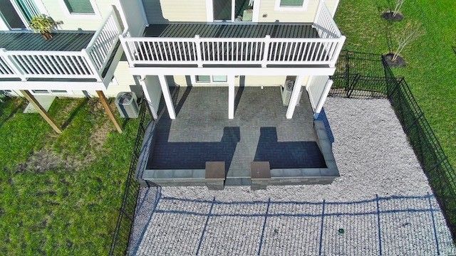 High-angle shot of a backyard patio with a deck above, surrounded by gravel and a fence.