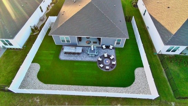 Aerial view of a backyard with patio, fire pit, green lawn, and white fence.