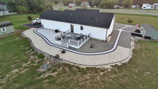 Aerial view of a white house with a gray deck, surrounded by gravel pathways and a small shed on the side.